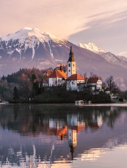 brown and white concrete building near lake and mountain under white clouds during daytime
